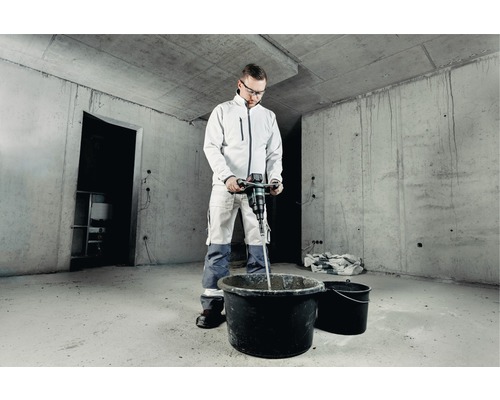 Remeselník mieša materiál elektrickým miešadlom na maltu v hrubej stavbe.