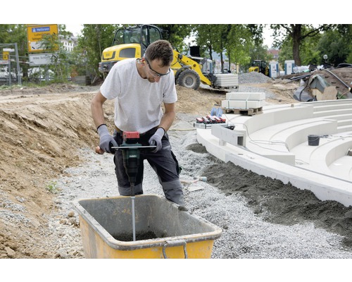 Muž mieša maltu s miešadlom na stavenisku.