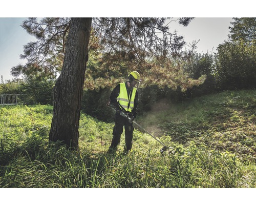 Muž v ochrannom odeve pracuje vonku s vyžínačom.