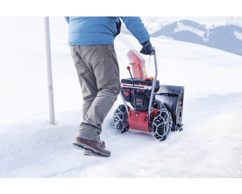 Osoba tlačí snehovú frézu na zasneženom povrchu.