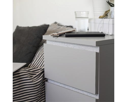 Sivá komoda so zásuvkami, na ktorej je mobilný telefón, powerbanka a pohár vody.