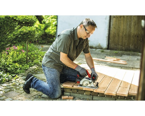 Muž reže drevo ručnou okružnou pílou v záhrade.