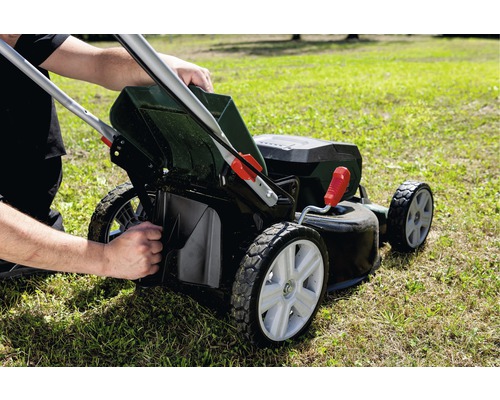 Osoba vyprázdňuje kôš na trávu kosačky na trávniku.