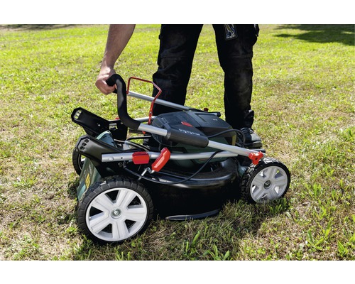 Osoba skladá kosačku na trávu s košom na trávu na trávniku.