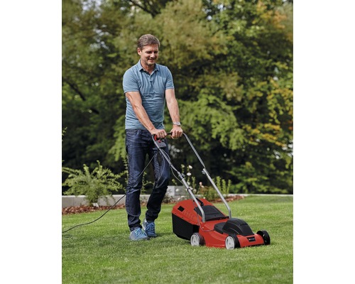 Muž kosí trávnik červenou elektrickou kosačkou na záhrade.