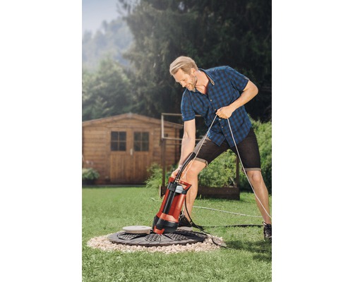 Muž obsluhuje ponorné čerpadlo v záhrade na odvodnenie šachty.