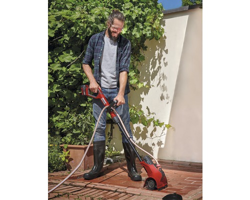 Muž používa akumulátorovú kefu na škáry v záhrade na odstraňovanie buriny medzi dlažobnými kameňmi.