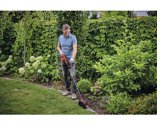 Muž strihá okraje trávnika zastrihávačom trávnika v záhrade.