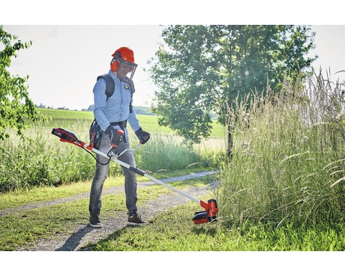 Muž strihá trávu akumulátorovým vyžínačom v záhrade.