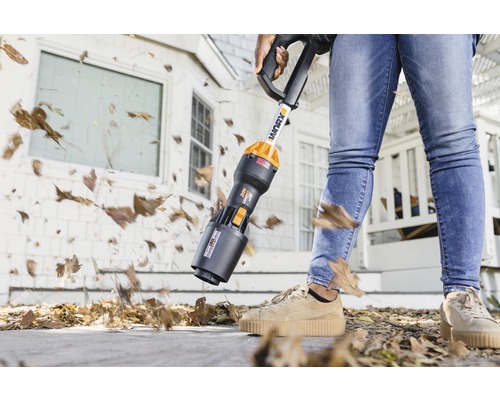 Osoba používa akumulátorový vysávač lístia na odstraňovanie lístia z chodníka.