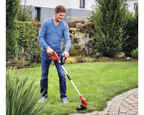 Muž strihá okraje trávnika akumulátorovým vyžínačom v záhrade.