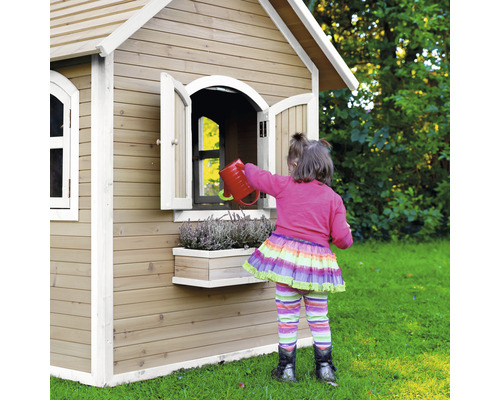 Dievča zalieva kvety pred dreveným detským domčekom v záhrade