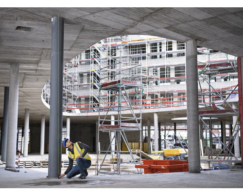 Stavebný robotník meria oceľový stĺp na stavenisku.
