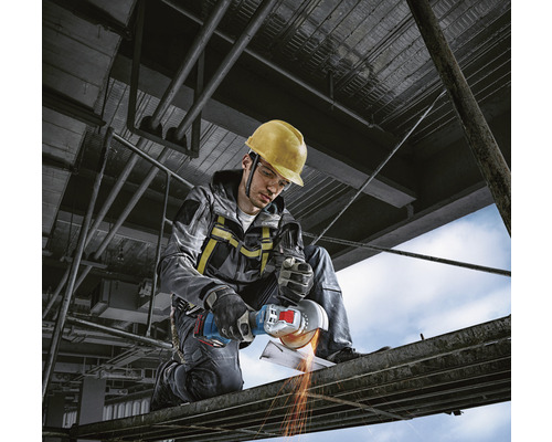 Robotník s ochrannou prilbou a uhlovou brúskou reže kov na stavenisku