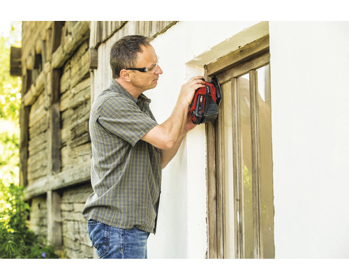 Muž s ochrannými okuliarmi renovuje drevené okno pomocou multifunkčného nástroja.