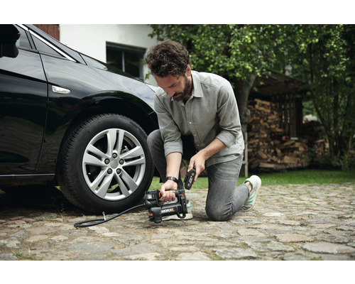 Muž plní pneumatiku auta prenosným kompresorom.