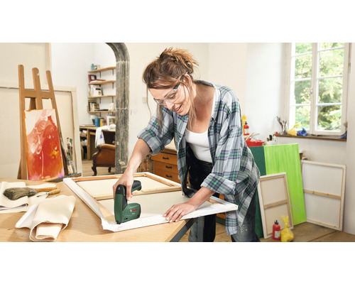 Žena používa elektrickú zošívačku na naťahovanie plátna v jasnom ateliéri.