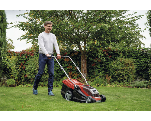 Muž kosí trávnik kosačkou na trávu v záhrade.