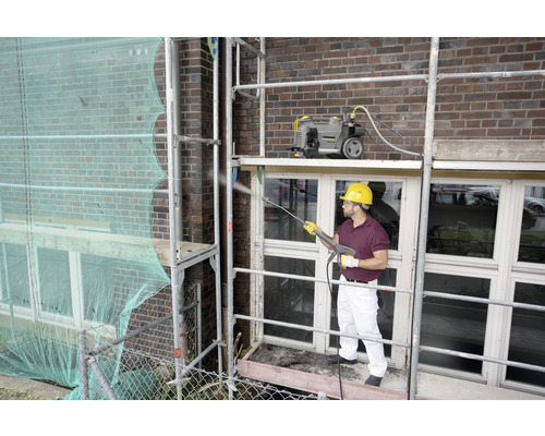 Muž na lešení čistí fasádu vysokotlakovým čističom