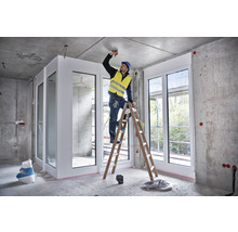 Interiérová scéna v hrubej stavbe s remeselníkom na rebríku pracujúcim na strope.