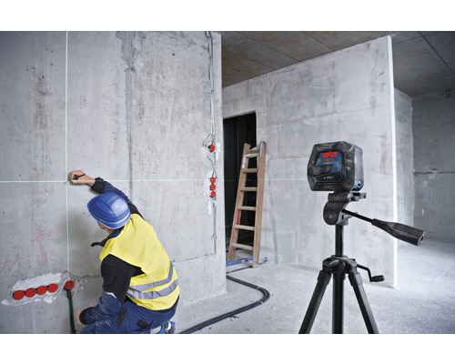 Pracovník označuje body na betónovej stene v hrubej stavbe pomocou krížového lasera.