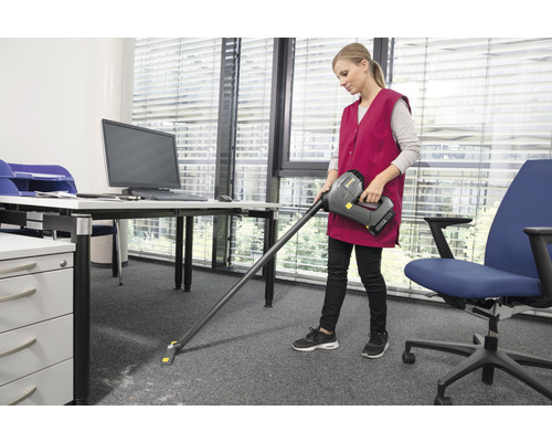 Žena vysáva koberec v kancelárii akumulátorovým vysávačom.