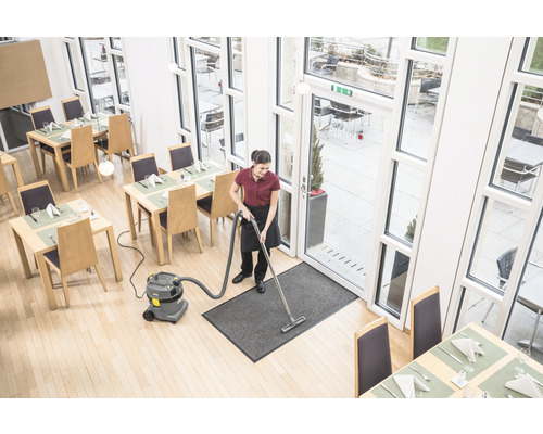 Upratovačka vysáva vstupný koberec v reštaurácii viacúčelovým vysávačom.