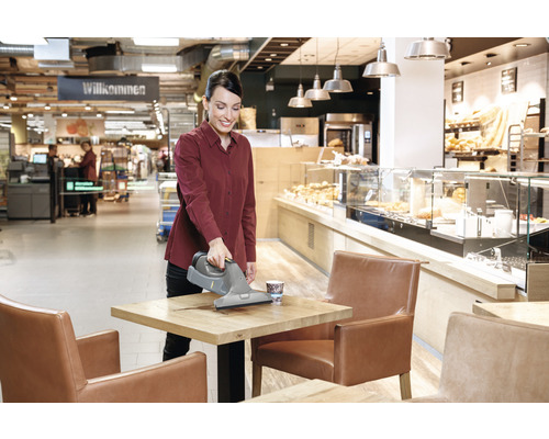 Žena čistí stôl s akumulátorovou okennou stierkou v kaviarni.