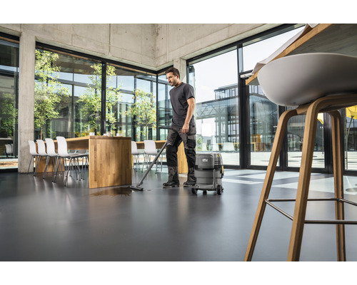 Muž čistí podlahu v kancelárii pomocou mokrého a suchého vysávača.