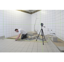 Obkladač pracuje s čiarovým laserom v kúpeľni s bielymi dlaždicami