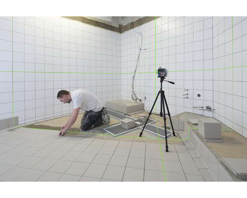 Obkladač pracuje s čiarovým laserom v kúpeľni s bielymi dlaždicami