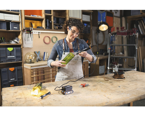 Žena vŕta otvor do sklenenej fľaše pomocou rotačného nástroja pre domácich majstrov v dielni.