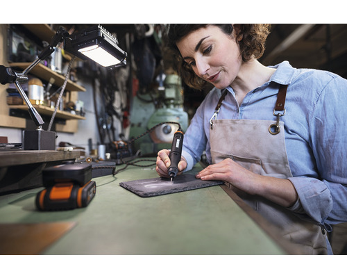 Žena gravíruje bridlicovú dosku gravírovacím strojom na pracovnom stole.