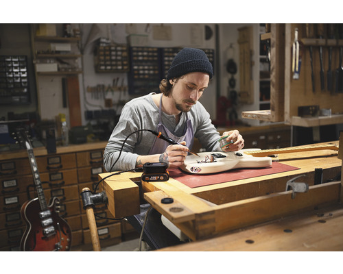 Muž spájkuje gitaru v dielni s spájkovačkou