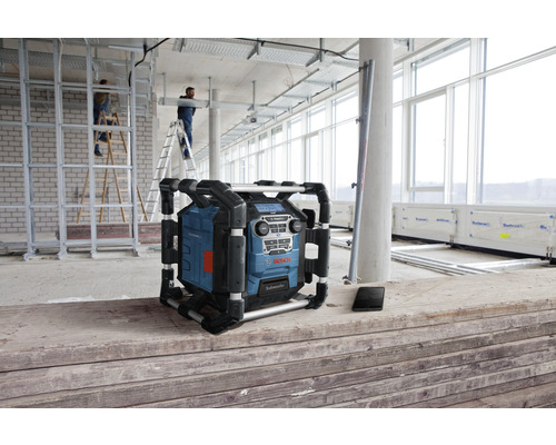 Staveniskové rádio Bosch na stavenisku so stavebnými robotníkmi a stavebnými materiálmi