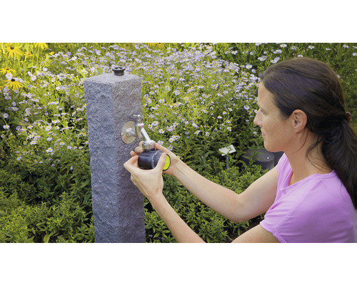 Žena pripája zavlažovací počítač k vodovodnému kohútiku v záhrade.