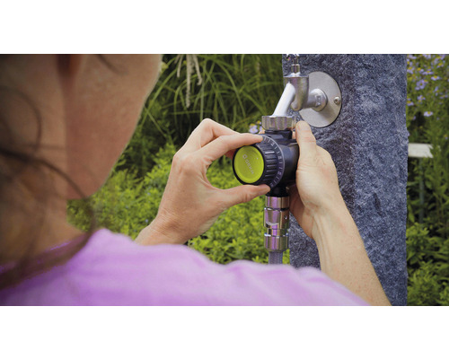 Žena ovláda zavlažovací počítač na vodovodnom kohútiku v záhrade.