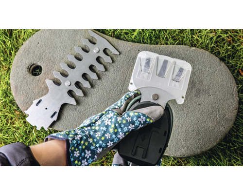 Ruka so záhradnou rukavicou drží orezávač nožníc na živý plot, vedľa zariadenia na zarovnávanie nožníc na živý plot