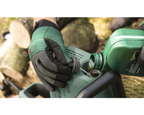 Osoba nalieva olej do reťazovej píly. V pozadí sú vidieť kusy dreva.