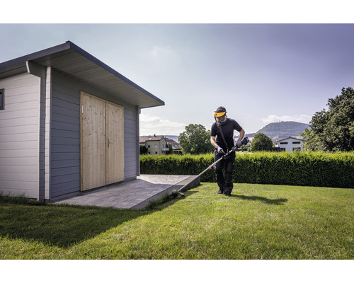 Muž strihá trávnik vyžínačom vedľa záhradného domčeka.