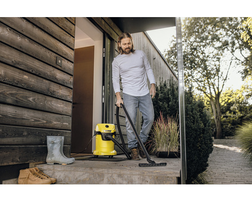 Muž čistí terasu pred domom mokro suchým vysávačom. V pozadí sú vidieť rastliny.