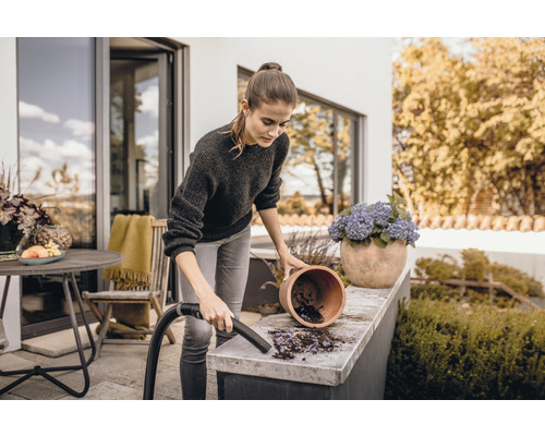 Žena vysáva nečistoty zo záhradného stola vysávačom.
