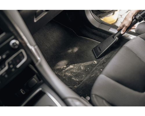 Osoba vysáva špinavý priestor pre nohy v aute pomocou vysávača.