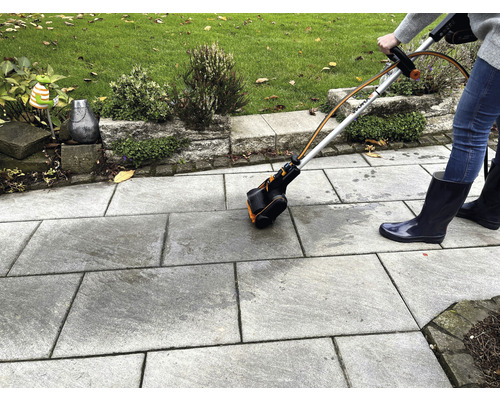 Osoba používa kefu na škáry na čistenie kamenných dosiek vonku.