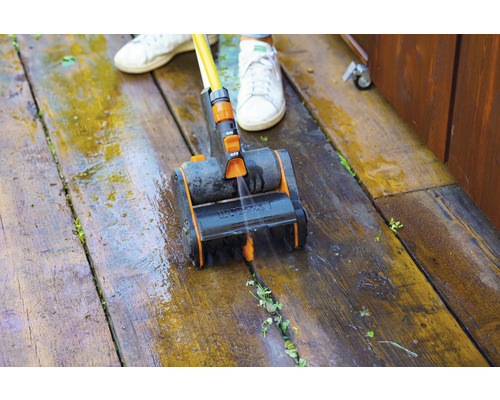 Osoba čistí drevenú terasu kefou a vodou.