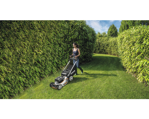 Žena kosí trávnik kosačkou v záhrade s bambusovými živými plotmi.