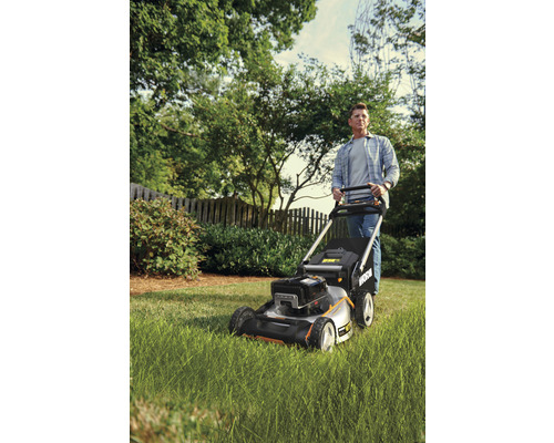 Muž tlačí kosačku na trávu v záhrade.