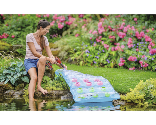 Žena inštaluje plávajúci jazierkový filter s akumulátorovým skrutkovačom na záhradné jazierko.