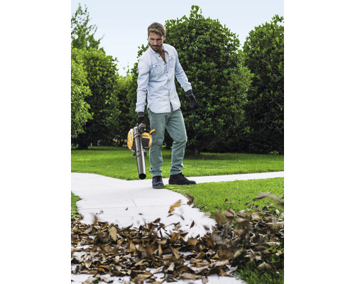 Muž používa žltý vysávač lístia v záhrade na odstránenie lístia.