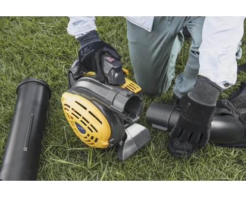 Osoba montuje žlto-šedý vysávač lístia na trávniku.